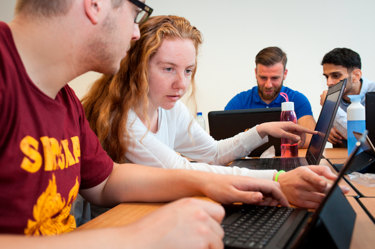 Twee studenten overleggen achter laptops in een klaslokaal