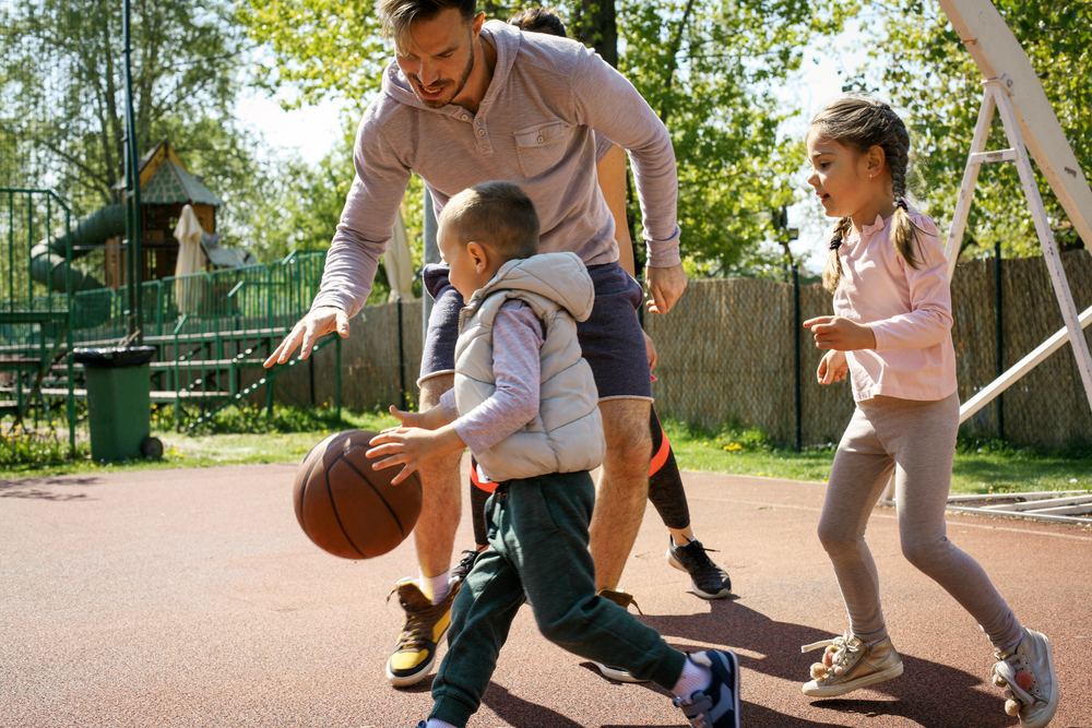 a man is playing basketball with two children, a young boy and a girl