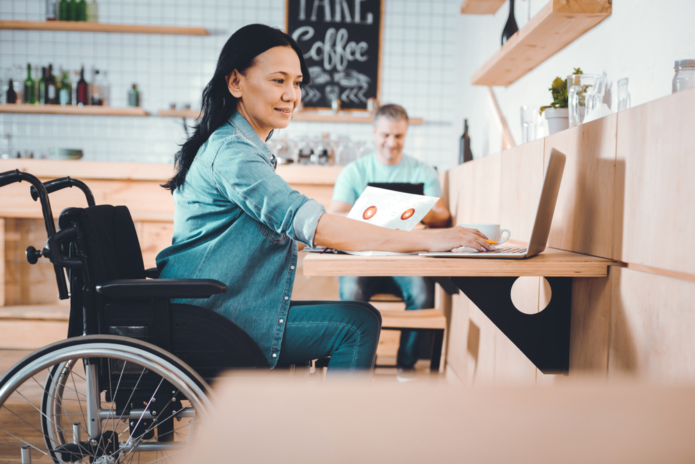 Woman in wheelchair searches for accessibility of public facilities on laptop