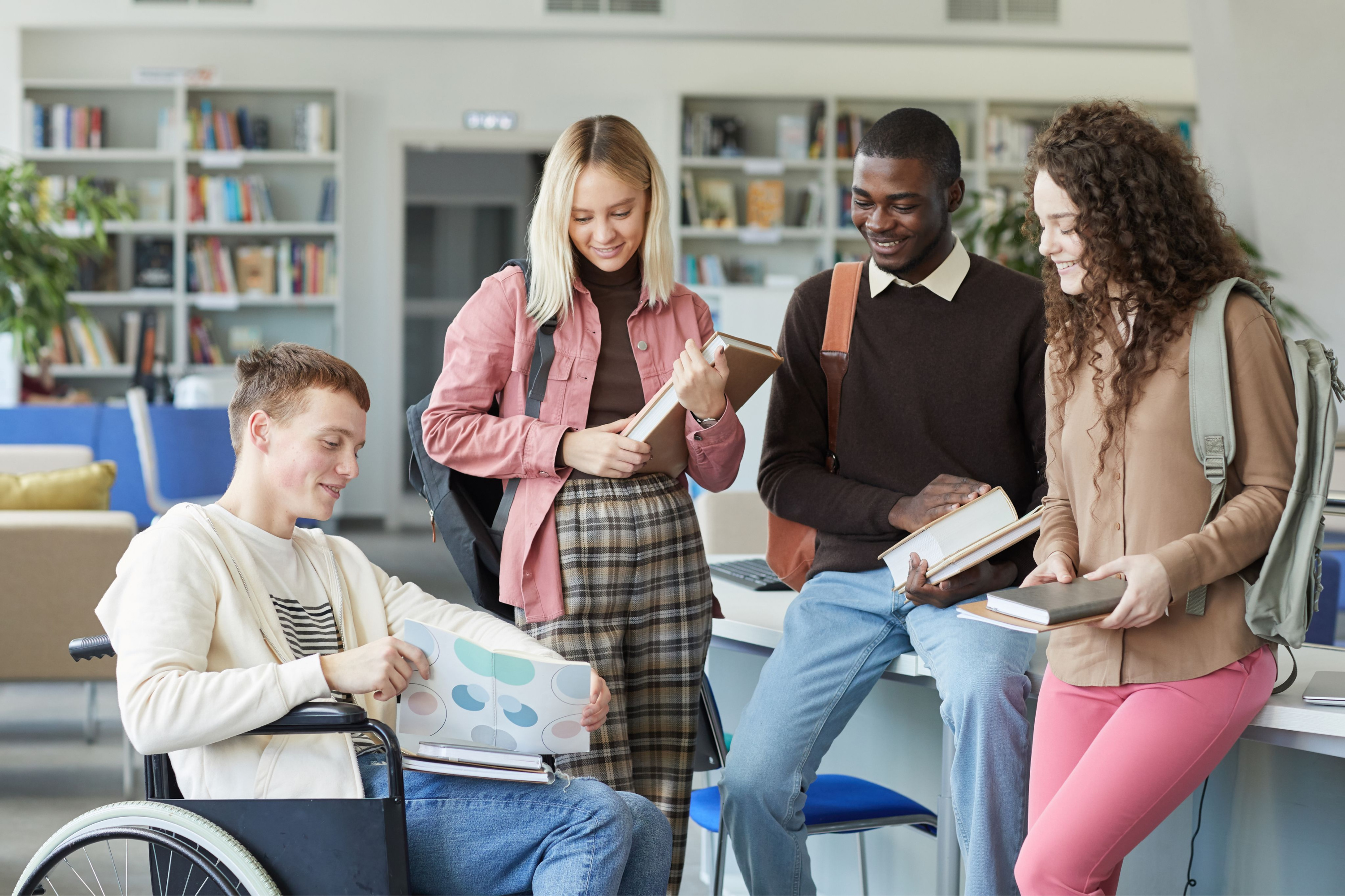 Inclusive Education, multi-etnische groep studenten in de bibliotheek met jongen in rolstoel op de voorgrond