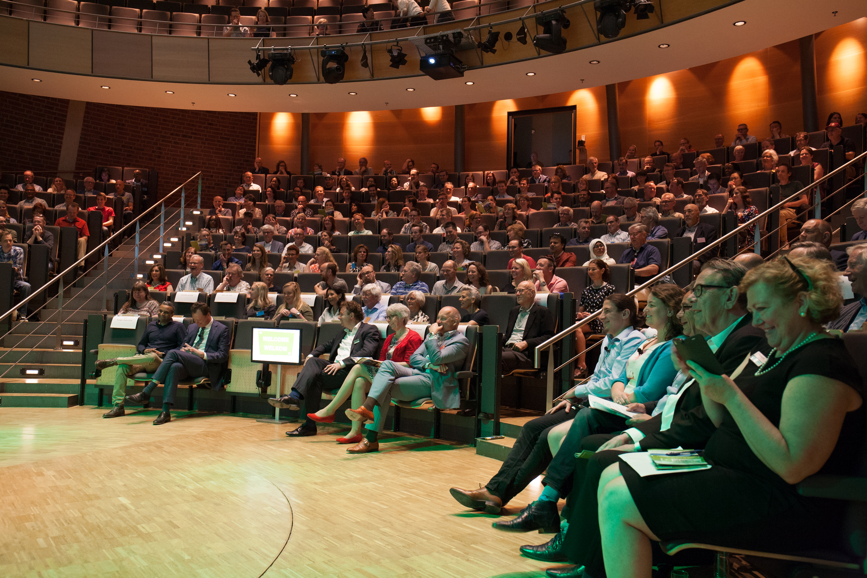 Publiek luistert aandachtig naar een presentatie in de aula