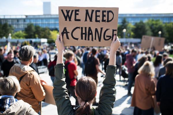 Vrouw met protestbord in de lucht met de tekst 'We need a change'