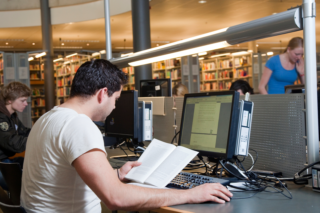 Student werkt achter een pc in de bibliotheek