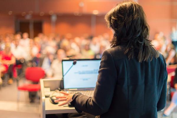 Vrouw achter een katheder praat voor publiek