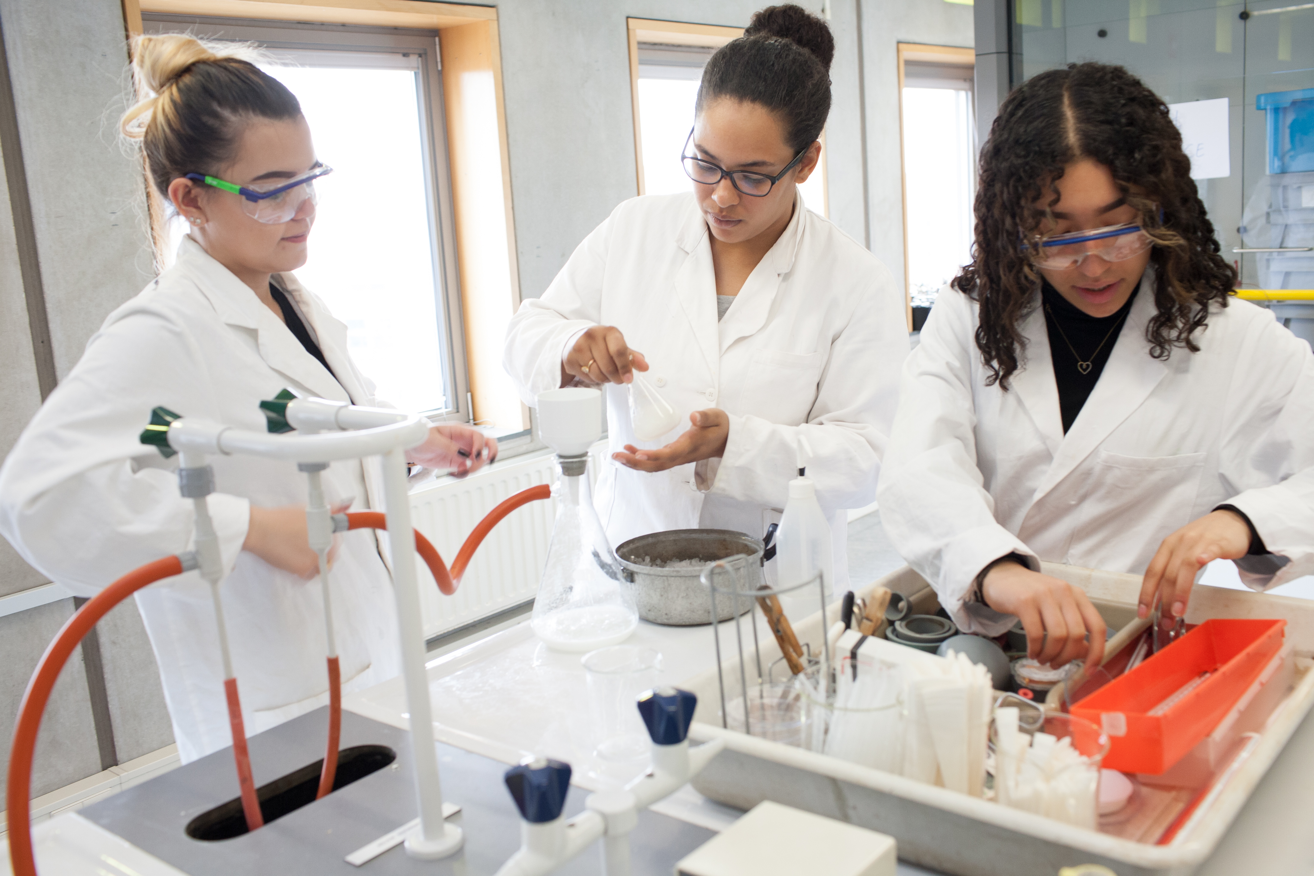 Drie studenten in labjassen werken aan praktijk