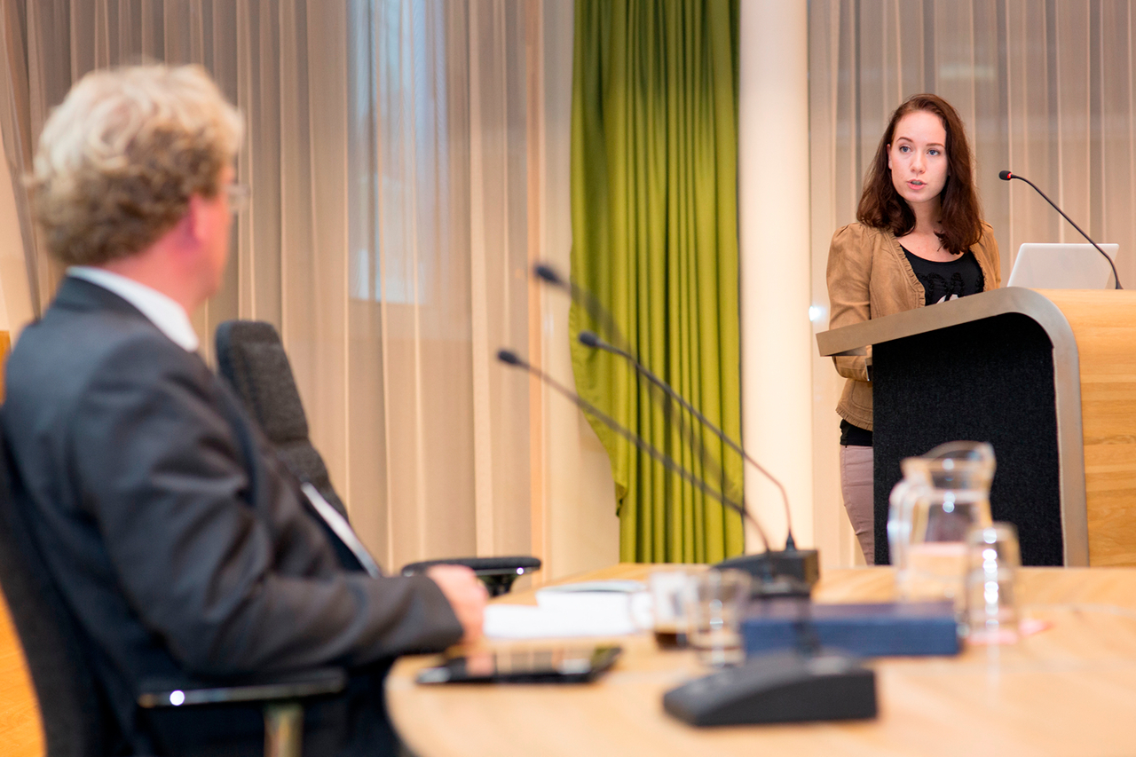 Studente staat achter katheder in overleg met een man in de raadzaal