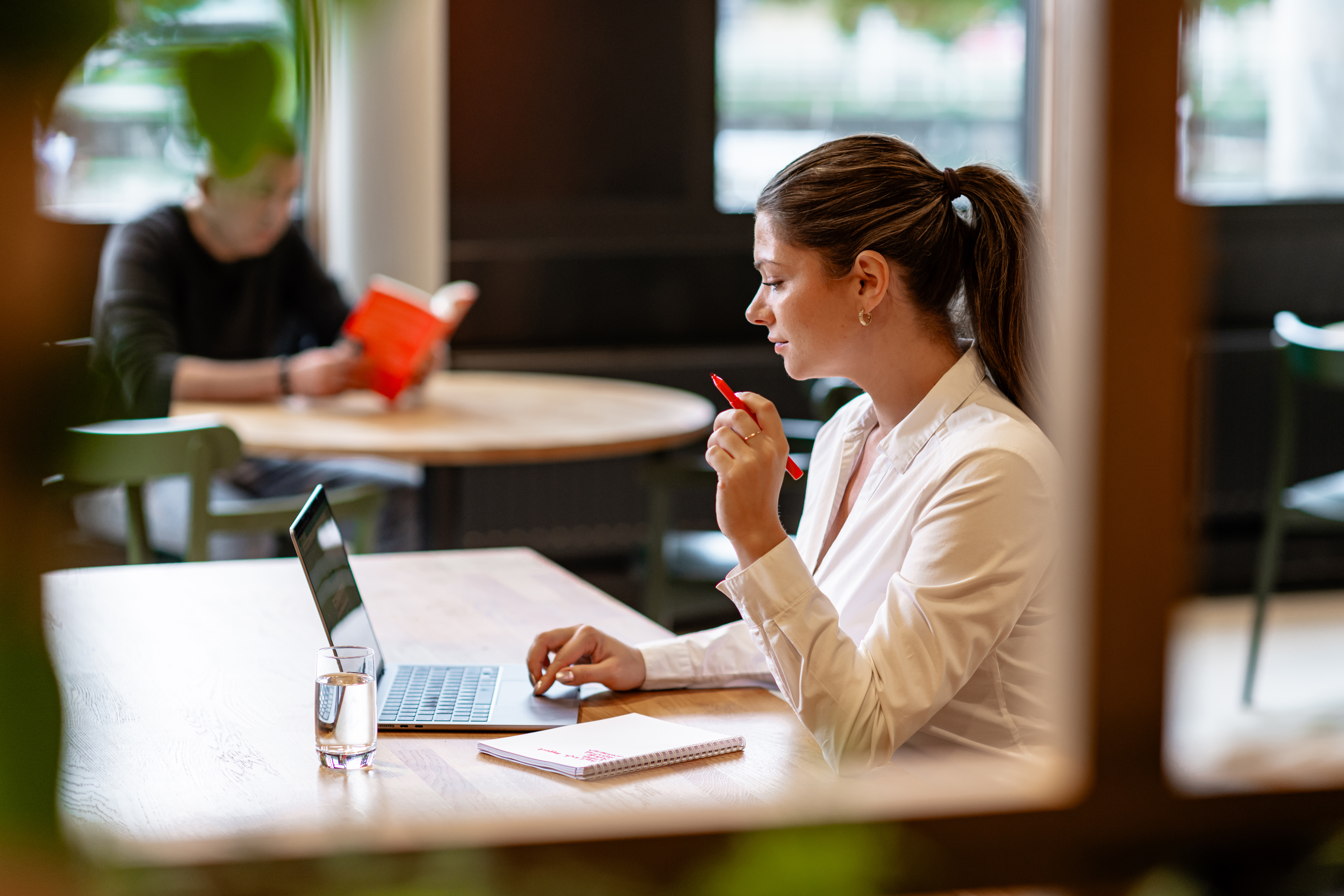 A women sitting behind a table with her laptop holding a red pen