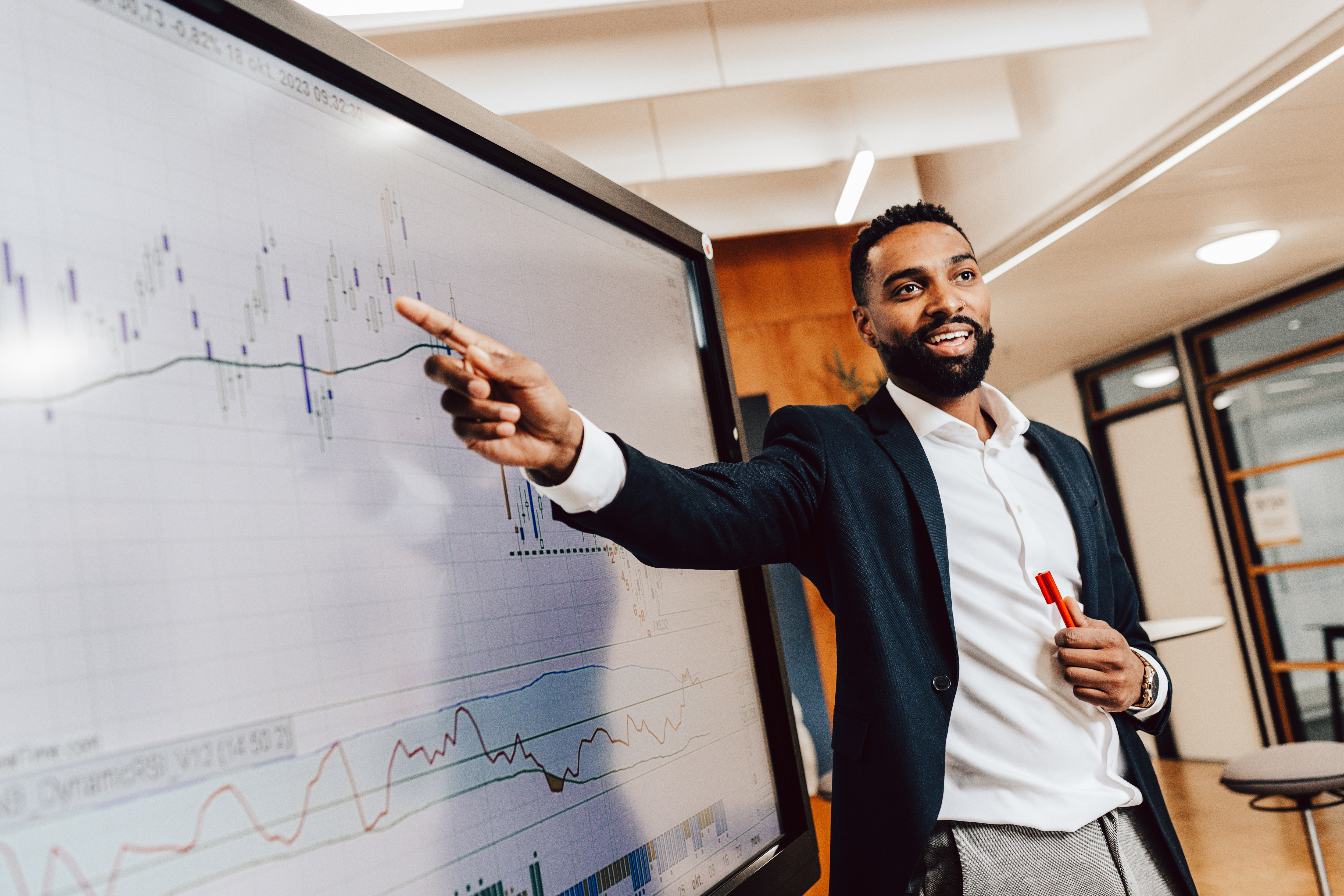 A male presenting on a whiteboard holding a red pen