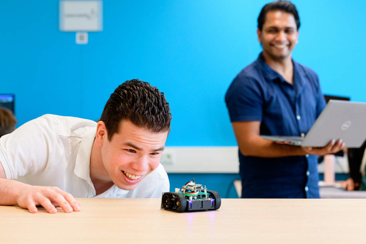 Student ICT kijkt blij naar voorwerp op tafel