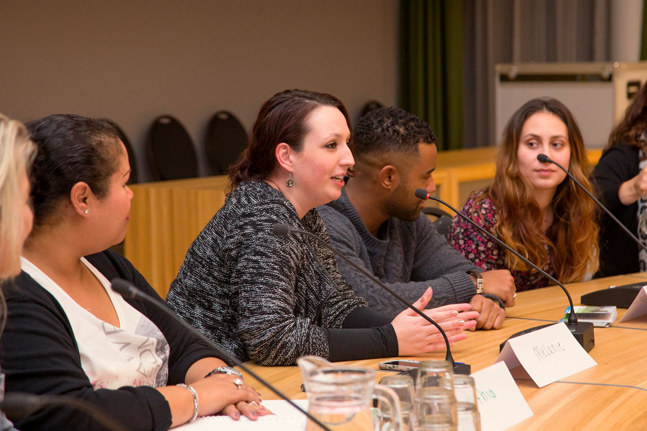 Studenten aan een vergadertafel tijdens een paneldiscussie; een vrouw spreekt in de microfoon.