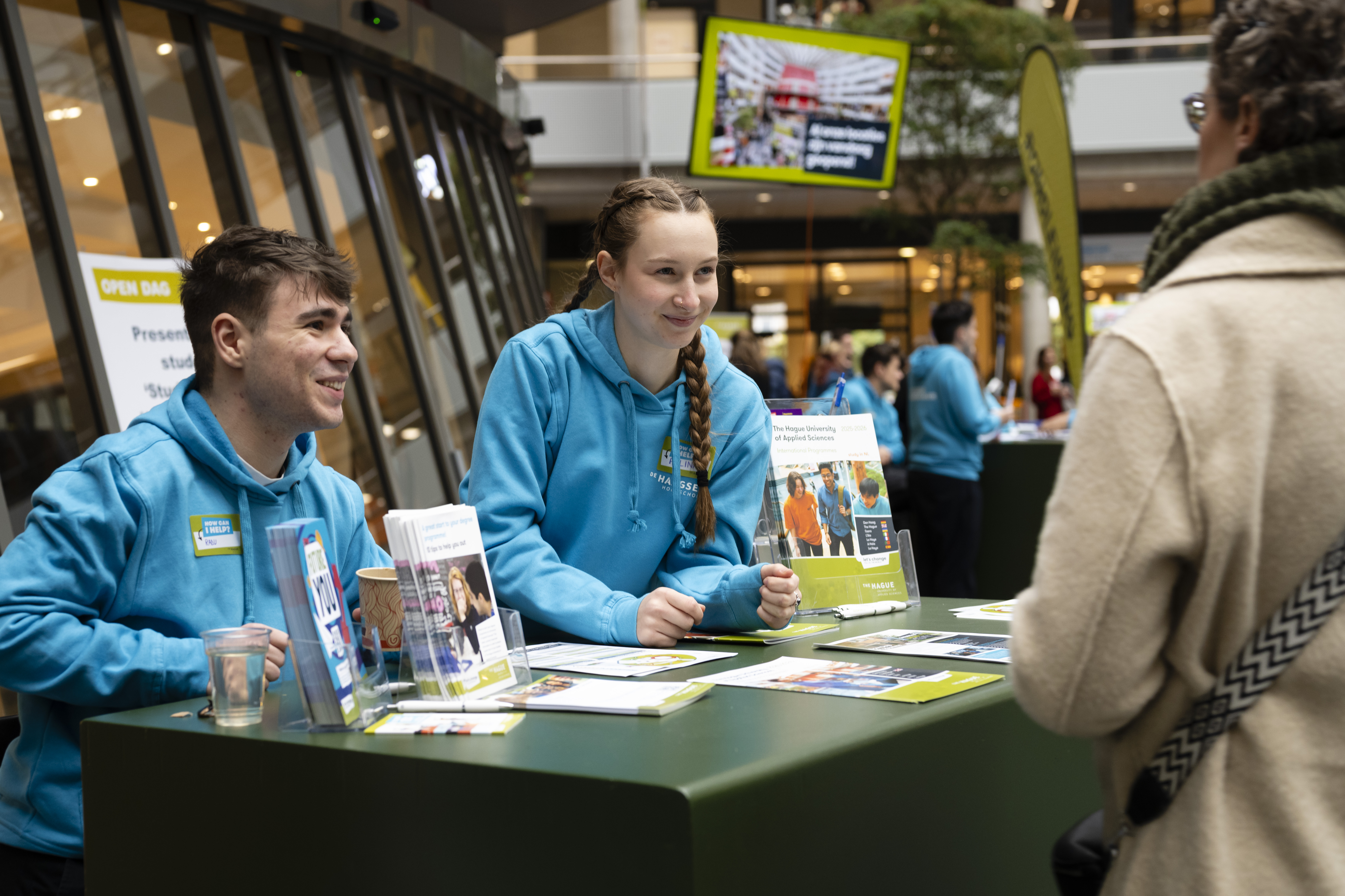Twee studenten achter een balie in gesprek met een bezoeker van de Open Dag