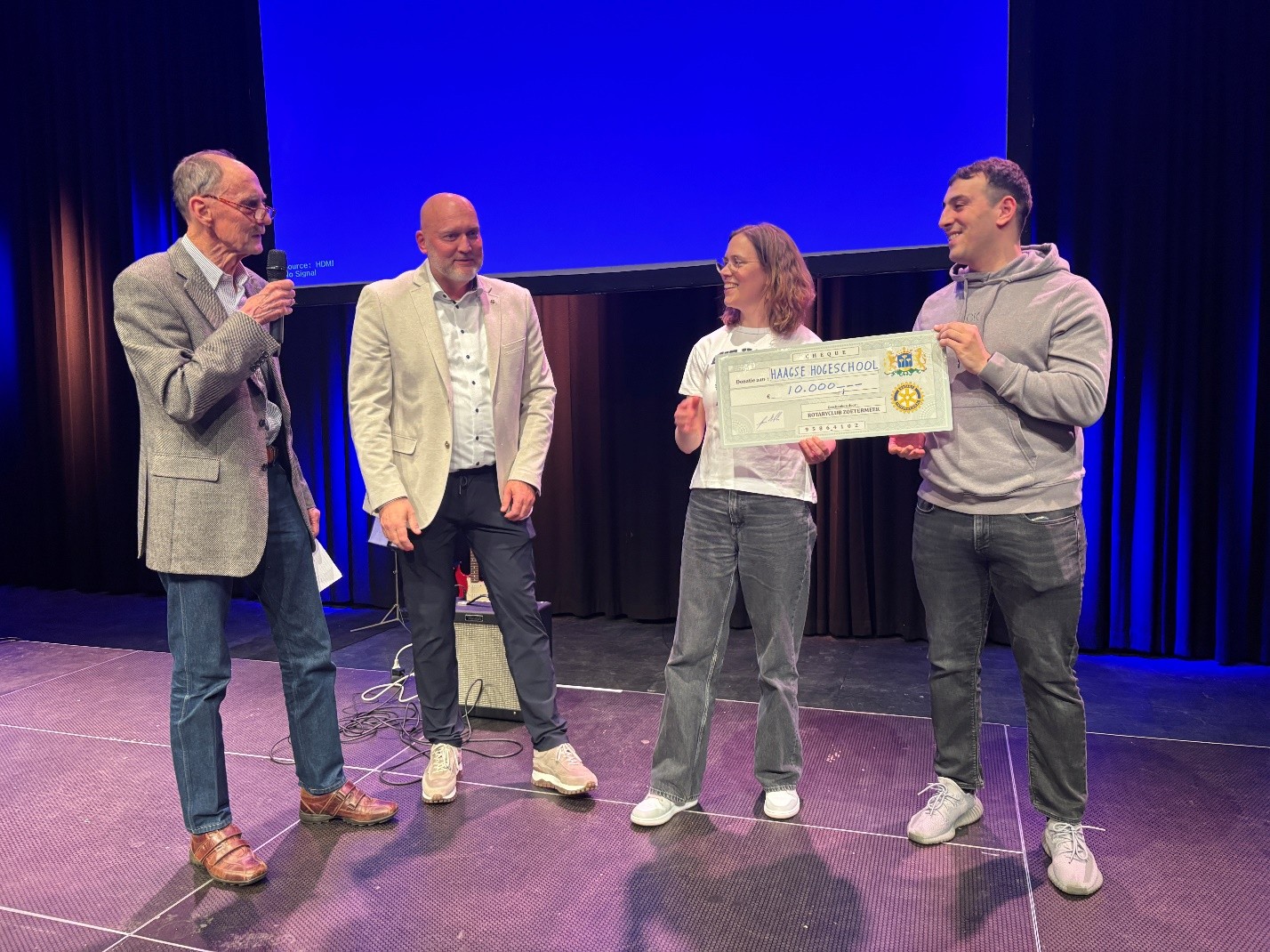 Vier personen staan op een podium en nemen een geldbedrag in ontvangs.