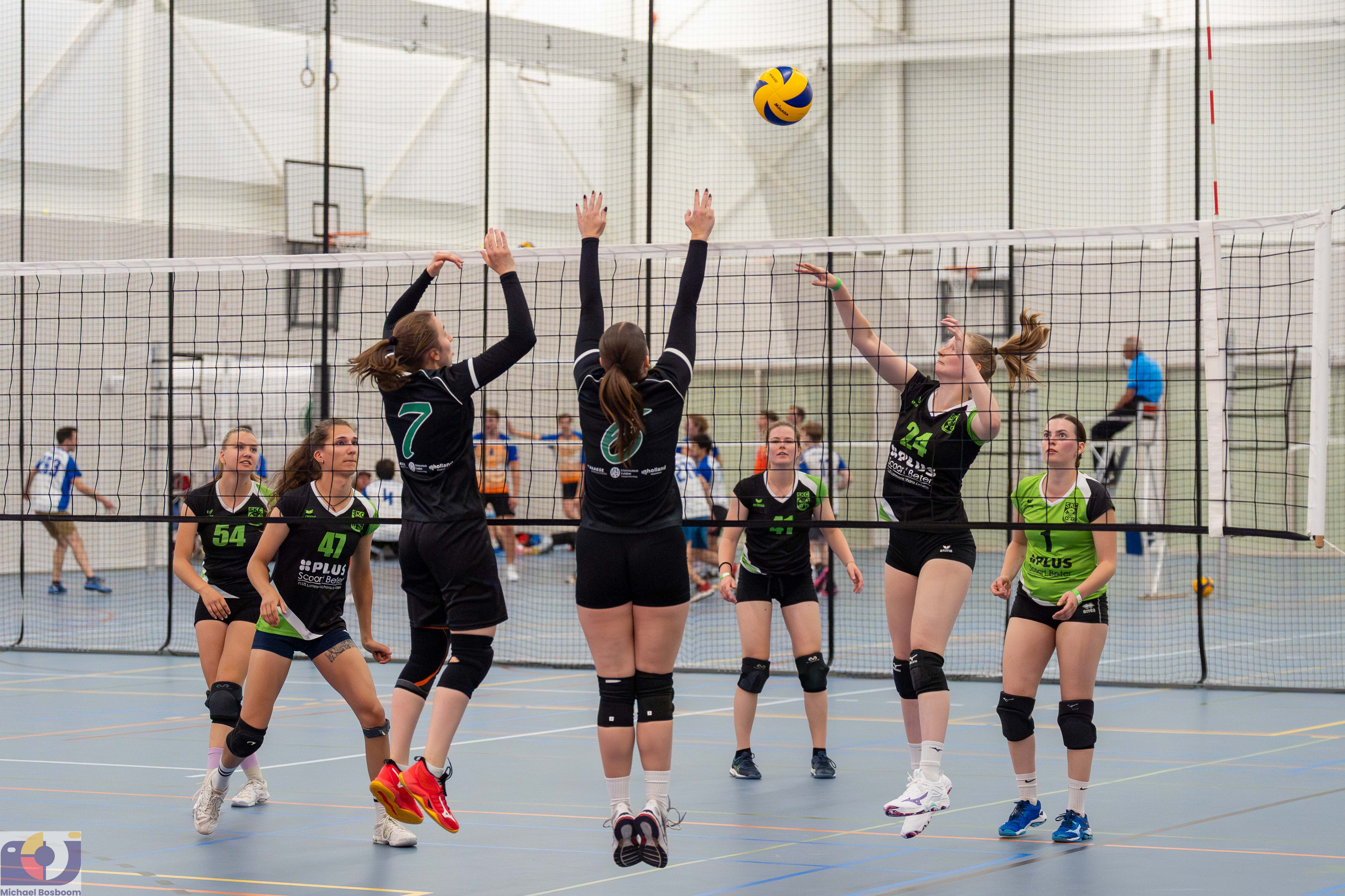 Volleybalspelers springen bij het net om de bal te blokkeren tijdens een zaalwedstrijd.