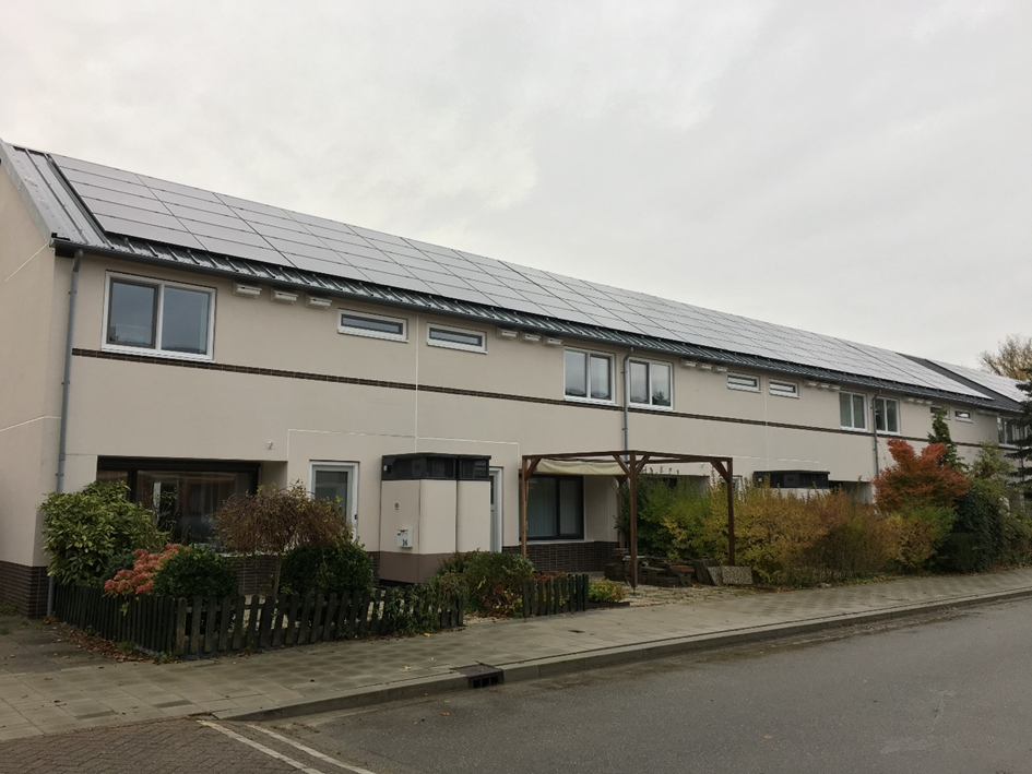 Rijtje woningen met zonnepanelen op het dak langs een rustige straat onder een bewolkte lucht.
