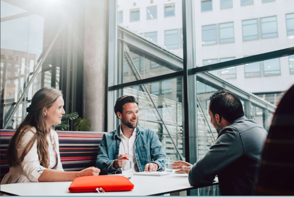 Three students collaborate around a table in a modern campus building with large windows, reflecting THUAS’s practice-oriented and international learning environment.